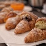 Selezione di cornetti freschi di pasticceria siciliana, incluso un cornetto con crema al pistacchio in primo piano.