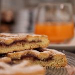 Primo piano di una fetta di crostata alla marmellata fatta in casa, con un bicchiere di succo d'arancia sullo sfondo.