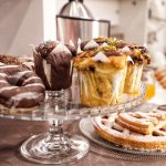 Alzata in vetro con muffin al cioccolato, ciambelle glassate e torte fatte in casa per la colazione degli ospiti.