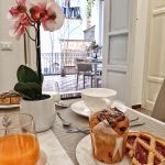 Dettaglio di un tavolo per la colazione apparecchiato all'interno, con muffin, crostata, succo e un'orchidea decorativa.